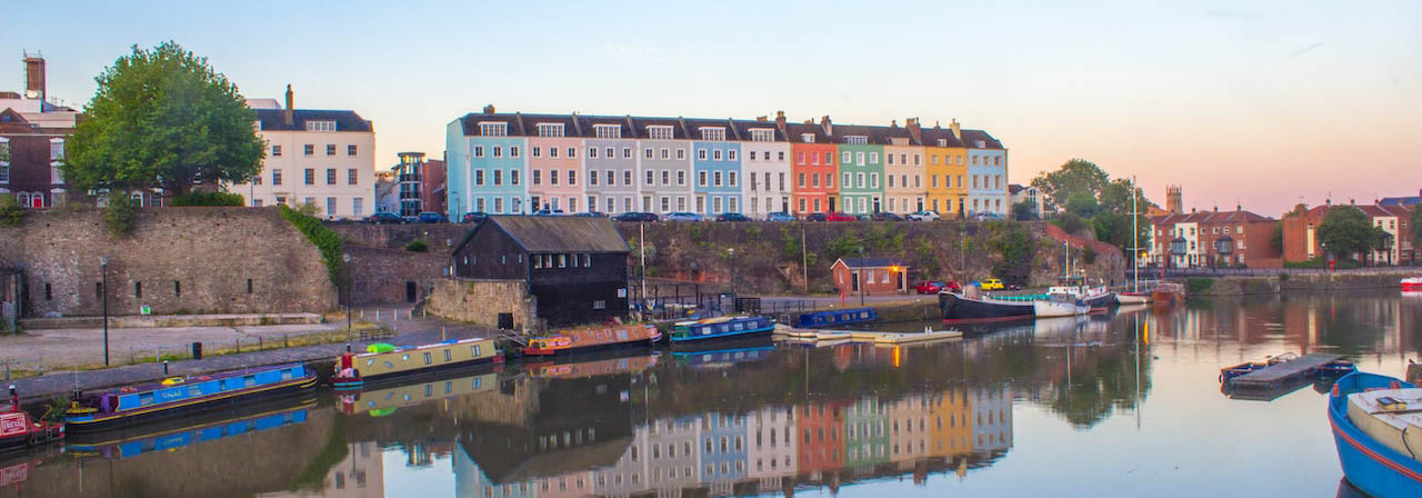A row of different colour houses on the waterfront, reflected in the river, at sunset