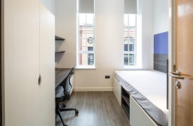 A room with a single bed against one wall and a desk and office chair opposite.