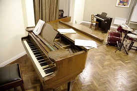 A room to play musical instruments. The room includes a piano and electric piano and a drum kit.