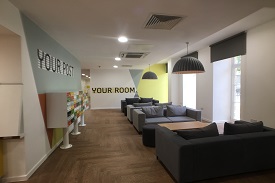 A room with several sofas and small coffee tables, and the words 'your room' painted on one wall. Another wall has some mailboxes attached and the words 'your post' painted on it.