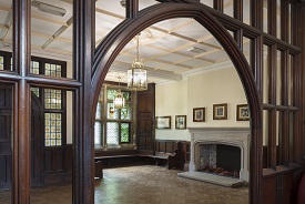 A hallway with wooden doors and panels, and fireplace and stained glass windows.
