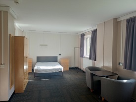 A 4ft bed in the background, wadrobe to the left and windows to the right with  two chairs and a table to the right.
