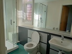 Shower cubicle to the right of the bathroom. Toilet to the right of the shower and basin to the right of the toilet. Large mirror on the back wall.