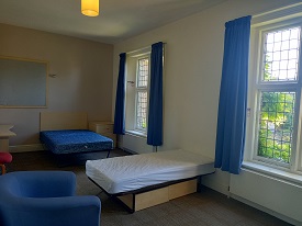 Two single beds to the left of the photo. A large window in the far right of the photo. Chair to the left of the photo.