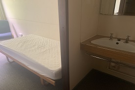 A room with a single bed, an armchair and a sink.
