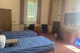 A room with two single beds, two desks with office chairs, an armchair and a cupboard.