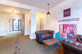 Hallway with two sofas around a coffee table, and a door leading outside at the far end. The wall by the sofas as 'Prestige student living #liveprestige' written on it.