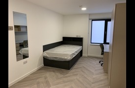 A large single bedroom with single bed, desk and chair, wardrobes and wall-mounted mirror.