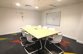 A table with eight chairs around it and a whiteboard on the wall nearby.