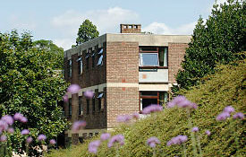 A three story University accommodation building with trees on each side and flowers in the foreground.