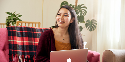 A female undergraduate student sitting on a sofa with a laptop and smiling.