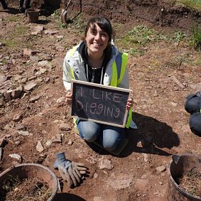 A student at an archaeological excavation site holding a sign "I like Digging".
