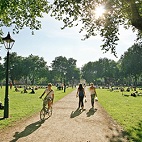 Queen's Square in the sun with people walking and cycling.