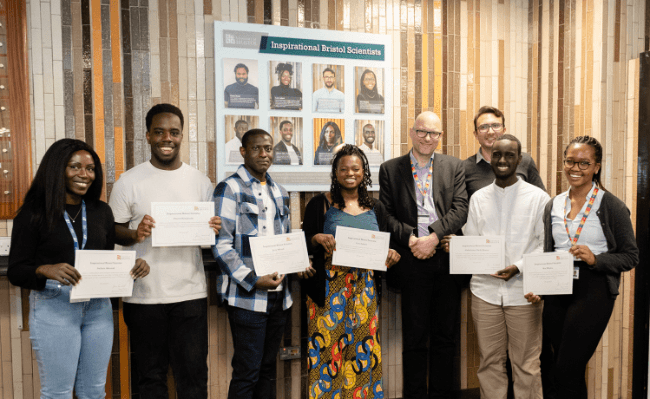 The 2023 celebrants with their certificates and Dean of Science, Jens Marklof, in front of the Inspirational Bristol Scientists board.