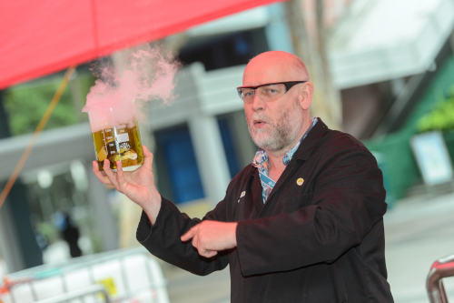 Tim Harrison holding a glass beaker of yellow smoking liquid.