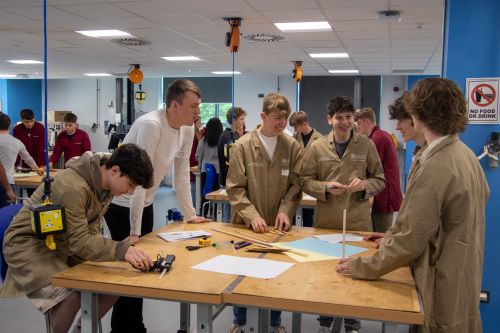 A group of five Sixth Form students are smiling while creating their wing design while a CDT student offers encouragement and advice. 
