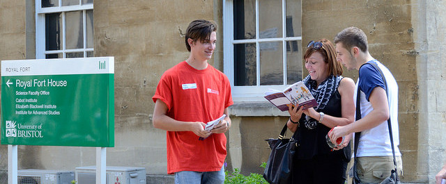 A student wearing a red University of Bristol t-shirt stewards a prospective student and their parent around the outside of Royal Fort House.