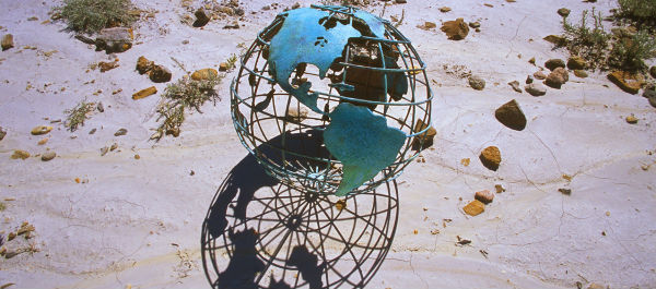 A wire globe of the world resting on beach 