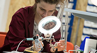 Female student in red lab coat using soldering equipment