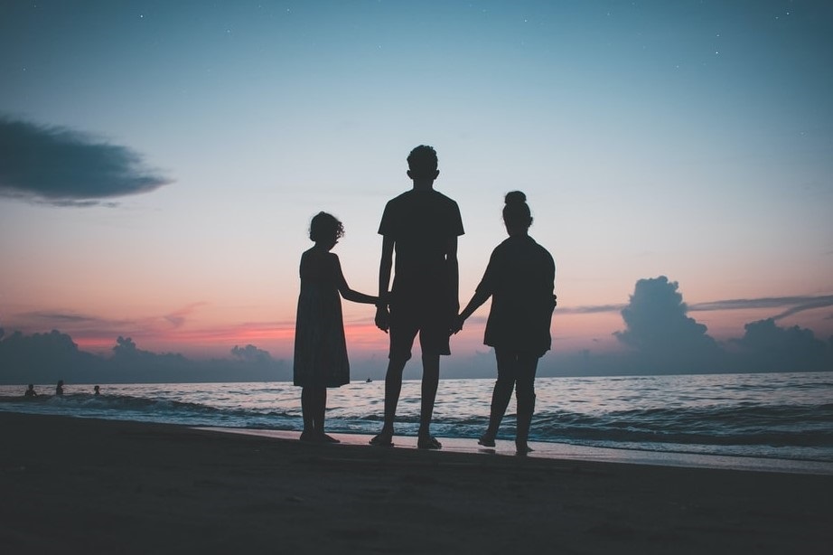 A silhouette image of a family standing on the beach and looking out to sea.