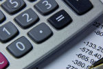 a close up photograph of a calculator and a ballpoint pen placed on a printed balance sheet.