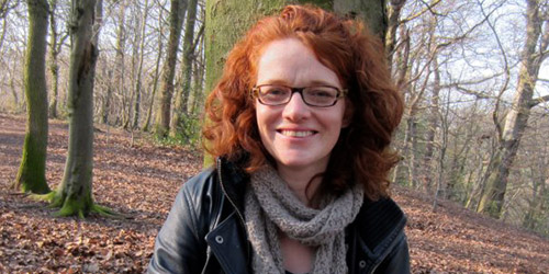 A woman smiling in an autumnal woodland.