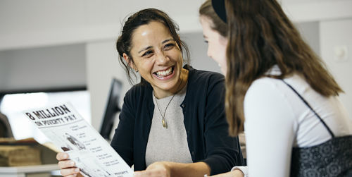 Two women share a joke as they discuss a leaflet about pay, while seated in an office. 