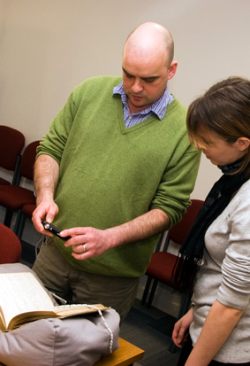 A lecturer photographs a manuscript document, while a student watches on