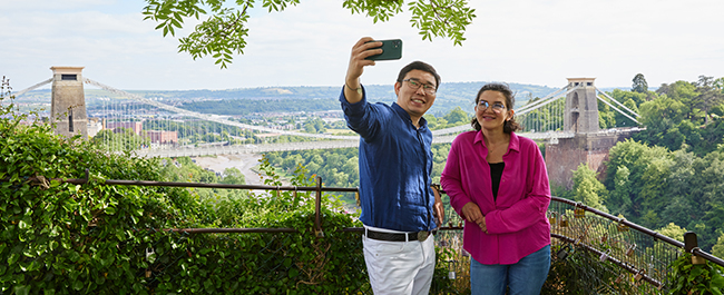Two students taking a selfie with Clifton Suspension Bridge in the background.