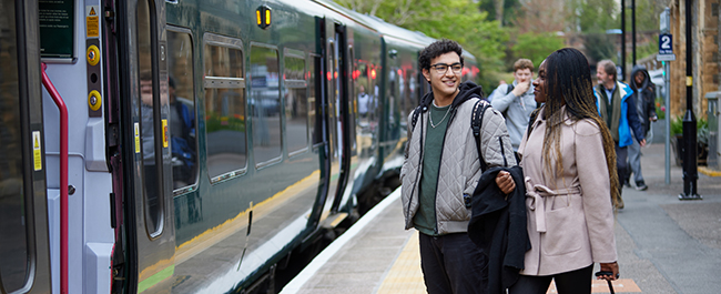 Two students standing on the platform as a train arrives.