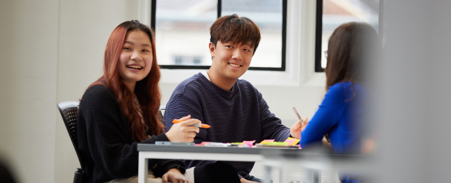 Two students working at a desk looking up and smiling.