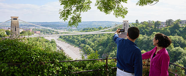 Two students looking out and taking a photo of Clifton Suspension Bridge.