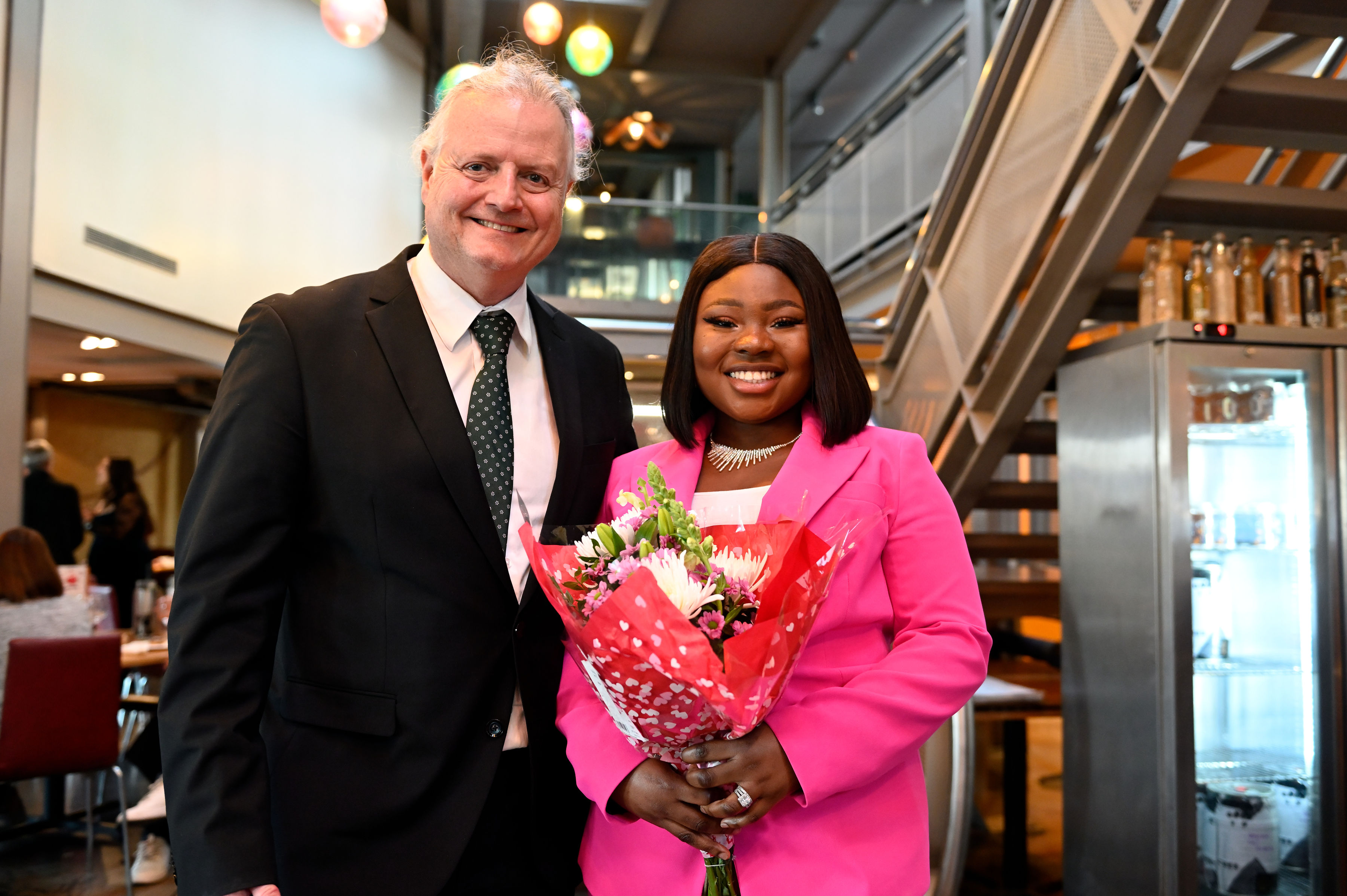 Prof Ken Oliphant, head of the University of Bristol Law School stood smiling next to a female law student prize wionner who is holding a bouquet of flowers and smiling.