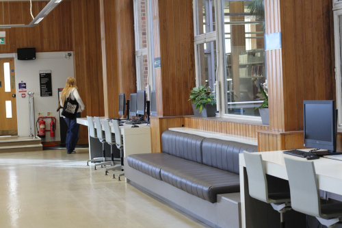 Woman walking down the main corridor in the Medical Library, the corridor includes computers, stools, sofas and windows.