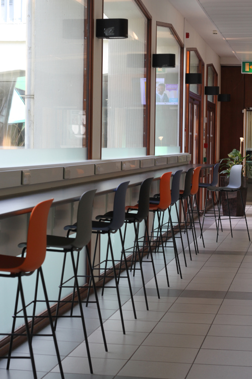 Row of high stool chairs running along a high desk table top facing a window 