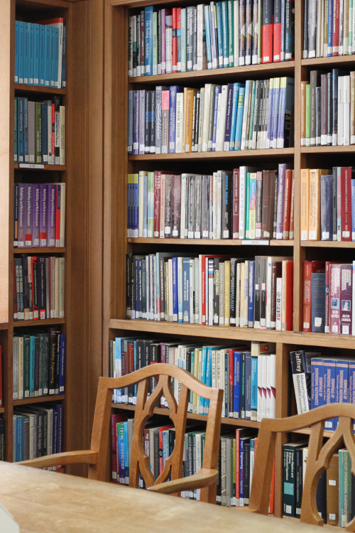 Two wooden chairs tucked under a wooden table, behind the chairs in a full bookcase.