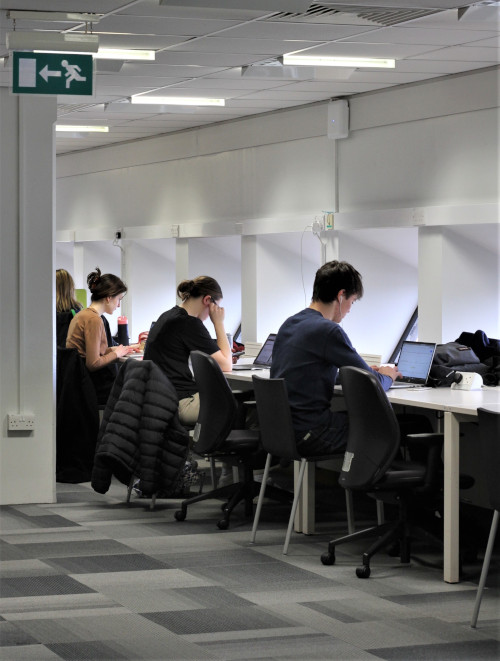 Three students in a row on one long white desk working on their laptops.