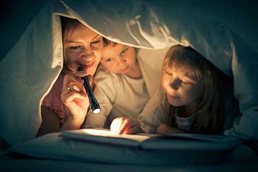 Image of a mother and children reading under the covers