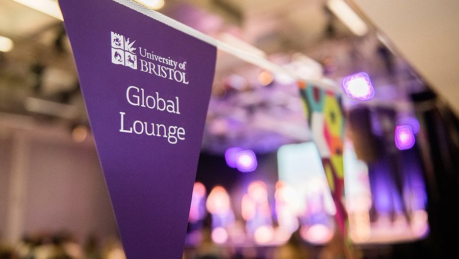 A purple triangular flag which says 'Global Lounge' in white writing, with UoB branding. It is part of a larger string of bunting. The background is blurred.