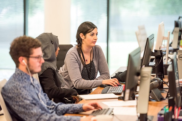 Three academics sitting at a bank of computers discussing what they see on one of the screens.