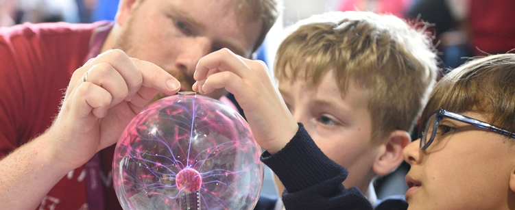 Two children and a researcher looking at a plasma ball at a FUTURES Research Fair. Credit: Bhagesh Sachania Photography