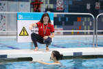 University of Bristol lifeguard poolside demonstrating a swimming movement to an individual in the pool 