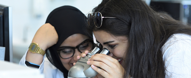 2 students in lab coats using a microscope together