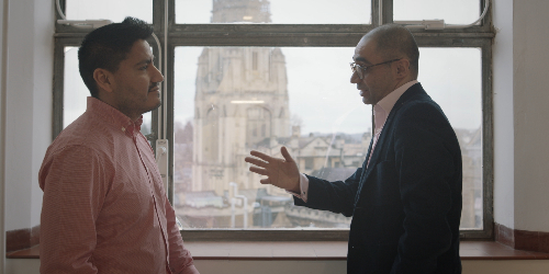 a student and staff member talking in front of a window with the Bristol skyline in view
