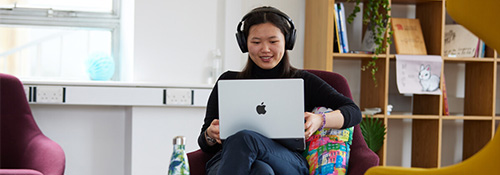 一名学生戴着耳机坐在笔记本电脑前，面带微笑地交谈