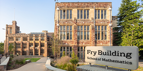 The exterior of an old building. A sign in front of it reads 'Fry Building School of Mathematics'.