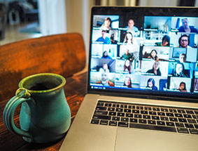 Laptop with video conference on-screen and a mug on the left.