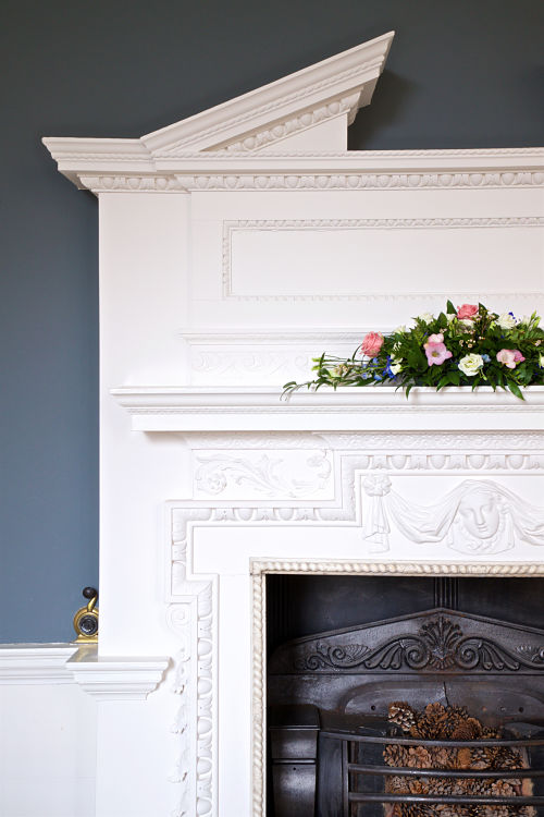 an ornate, white face place with flower arrangement no the mantelpiece. 