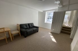A room with a table with chairs around it, and a sofa next to it. There are three steps up from the room to a corridor.