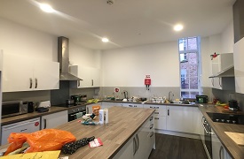 A communal kitchen with two ovens and hobs, two sinks, a fire blanket and lots of cupboards and drawers.